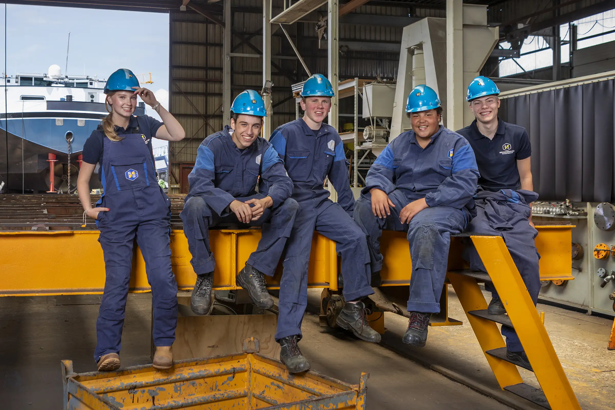 5 jongeren in werkkleding en helm van scheepsbouwer Nieuwenhuijsen zitten op een gele stalen balk.